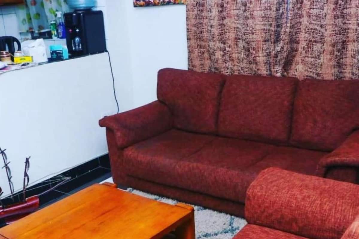 A living room with a red sofa, a wooden coffee table, and a kitchen area in the background.