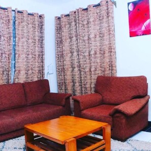 Relax in this inviting living room with a sofa set and coffee table, surrounded by patterned curtains and a beautiful artwork.