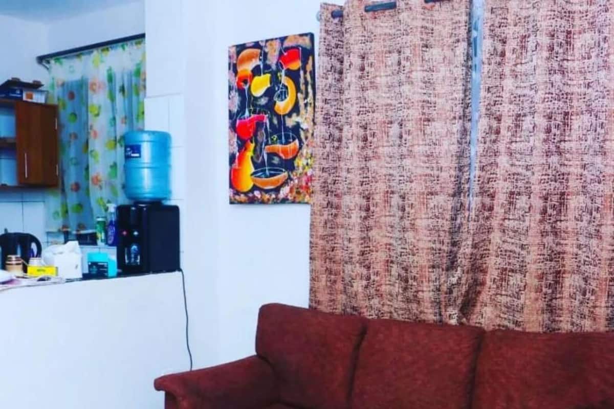 A living room with a red sofa, a wooden coffee table, and a kitchen area with a water dispenser and a coffee machine.