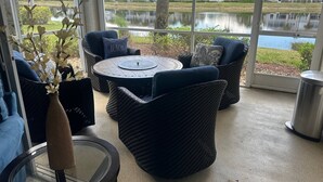 En patio med fletmøbler, et rundt bord og udsigt til et sø.