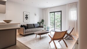 A modern living room with a sofa, coffee table, and a chair. There is a window with curtains, a plant, and a framed picture on the wall. - Marvelous 2BR Apartment with balcony  B (Athens)