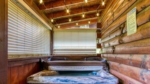 A wooden cabin interior with a hot tub, wooden walls, and a window with blinds. - Little Slice of Heaven -1BR 1BA Close to Town and Resort Amenities (Sevierville)