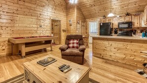 A cozy cabin interior with a pool table, a comfortable armchair, a dining area, and a kitchen with wooden cabinets and appliances. - Little Slice of Heaven -1BR 1BA Close to Town and Resort Amenities (Sevierville)