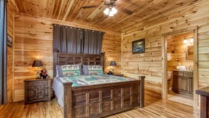 A wooden cabin bedroom with a bed, two nightstands, a ceiling fan, and a door leading to a bathroom.