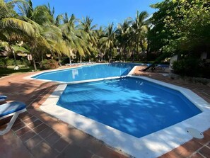 A swimming pool with a tiled deck, surrounded by palm trees.