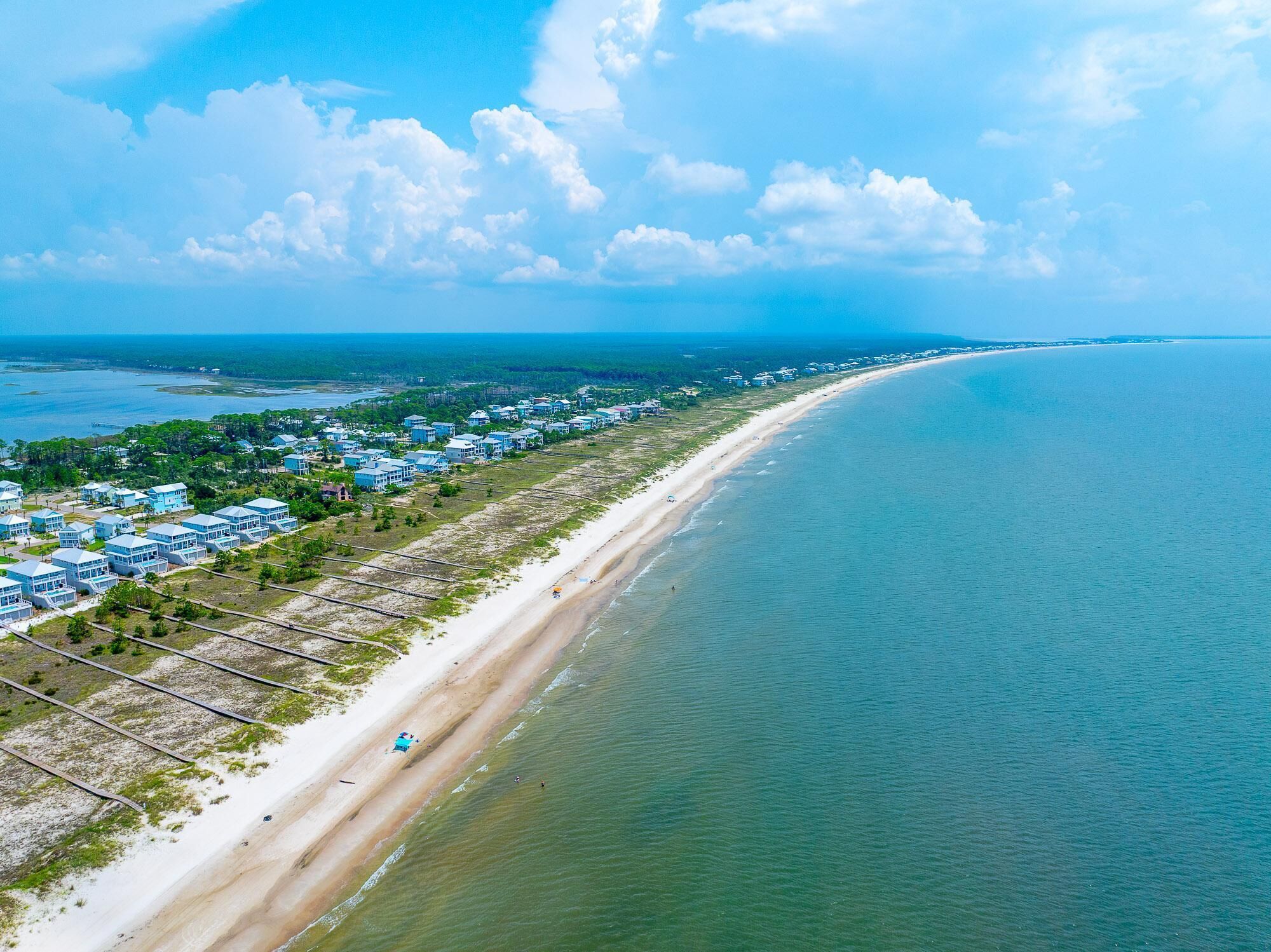 A coastal area with a long sandy beach and a row of buildings along the shore.