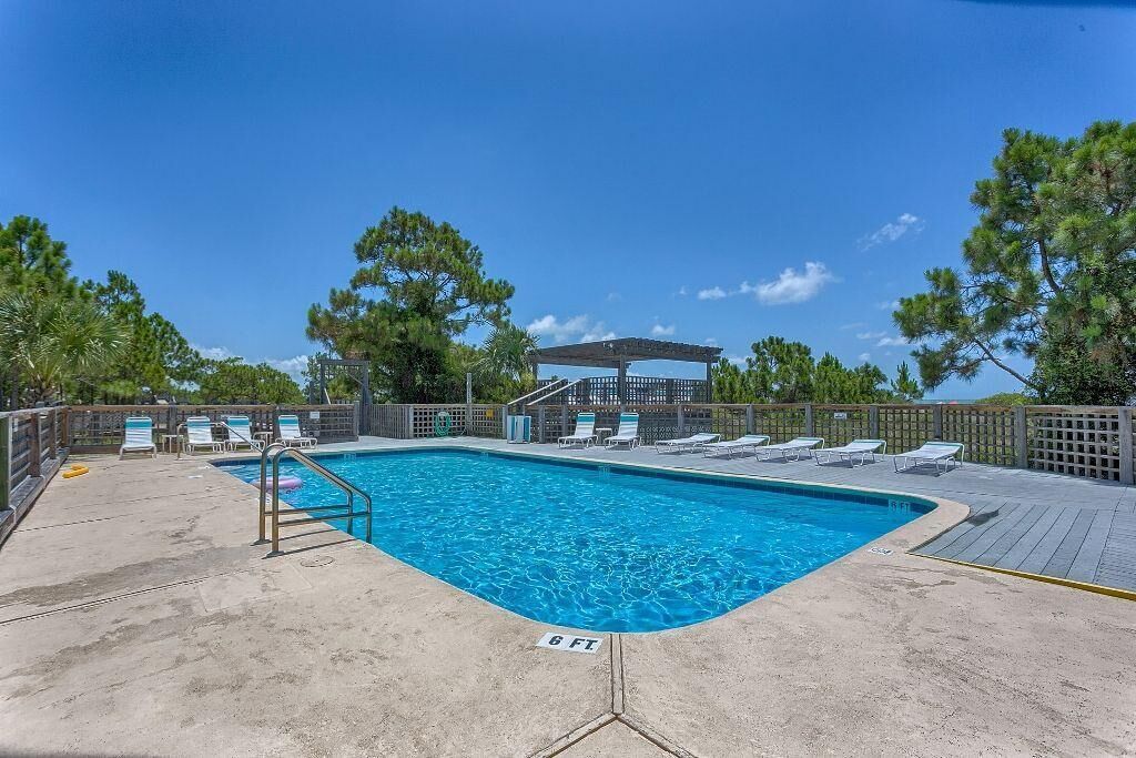 A rectangular swimming pool with a wooden deck surrounding it, equipped with lounge chairs and a covered seating area.