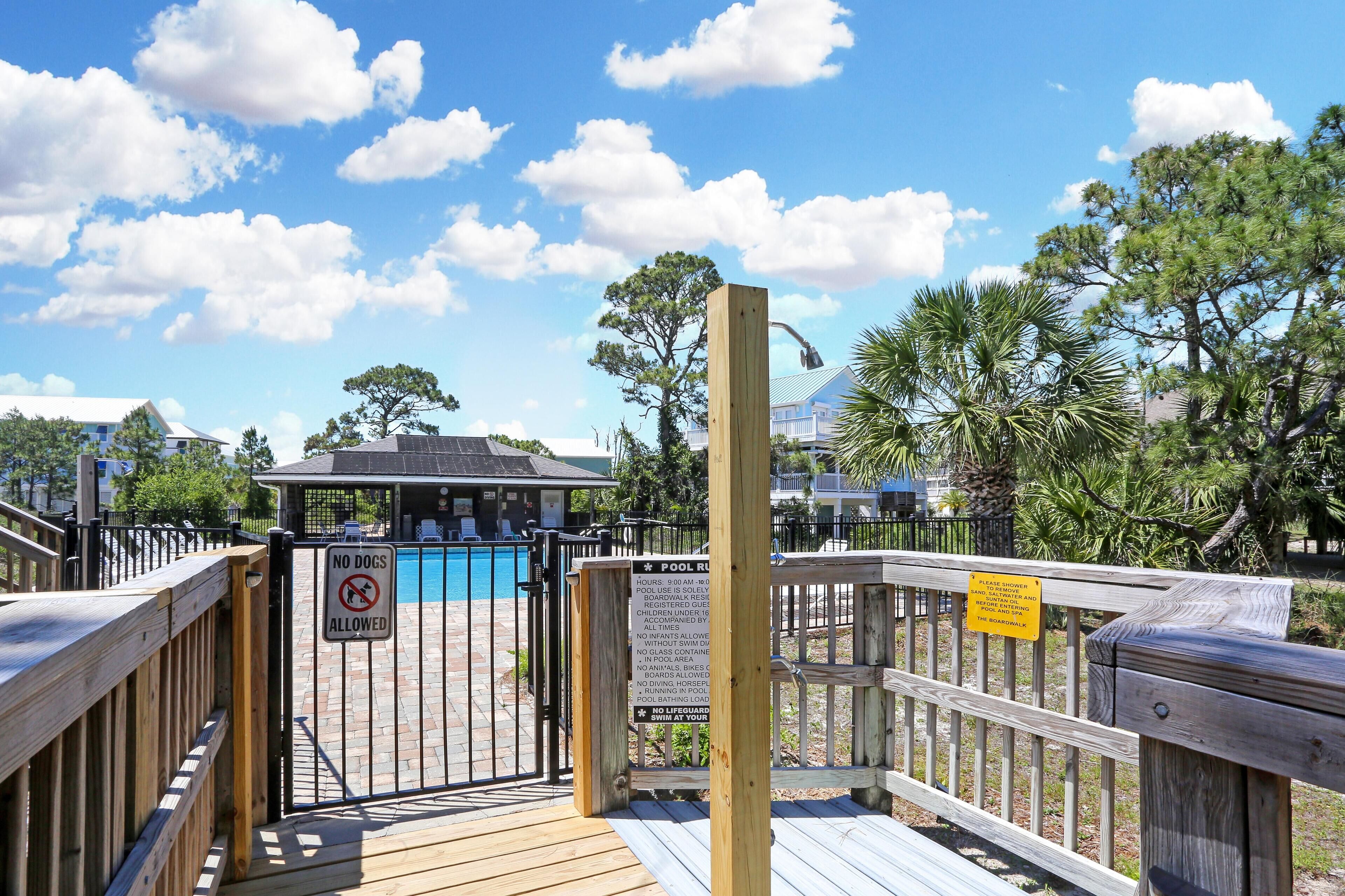 A wooden deck leading to a pool area with a sign prohibiting dogs.