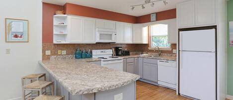 A modern kitchen with white cabinets, a granite countertop, and a built-in microwave.