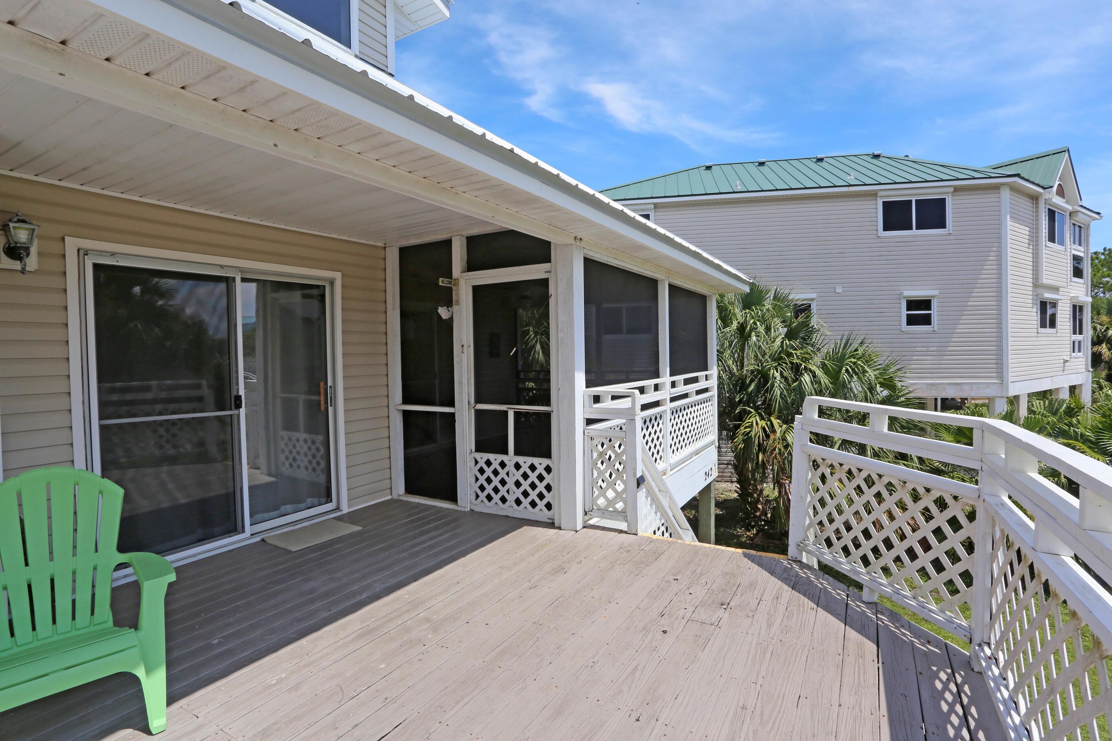 A covered porch with a green chair, a sliding glass door, and a white fence.