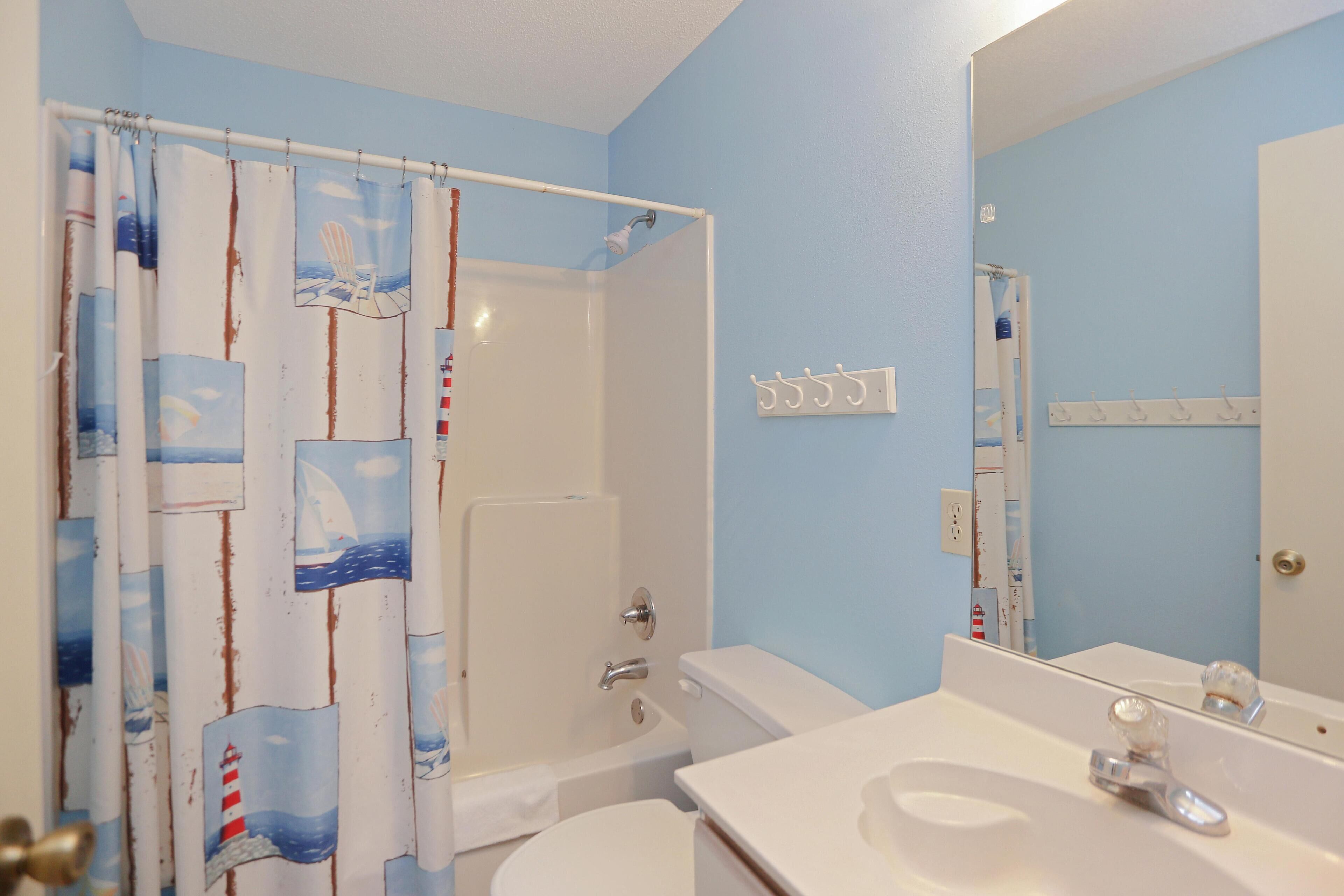 Ein Badezimmer mit Duschvorhang mit nautischen Motiven, einer Badewanne, einer Toilette, einem Waschbecken mit Spiegel und einem Handtuchhalter an der Wand.