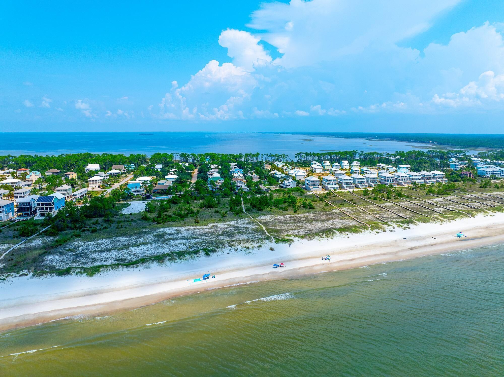 An aerial view of a coastal residential area with houses, a beach, and a clear sky.