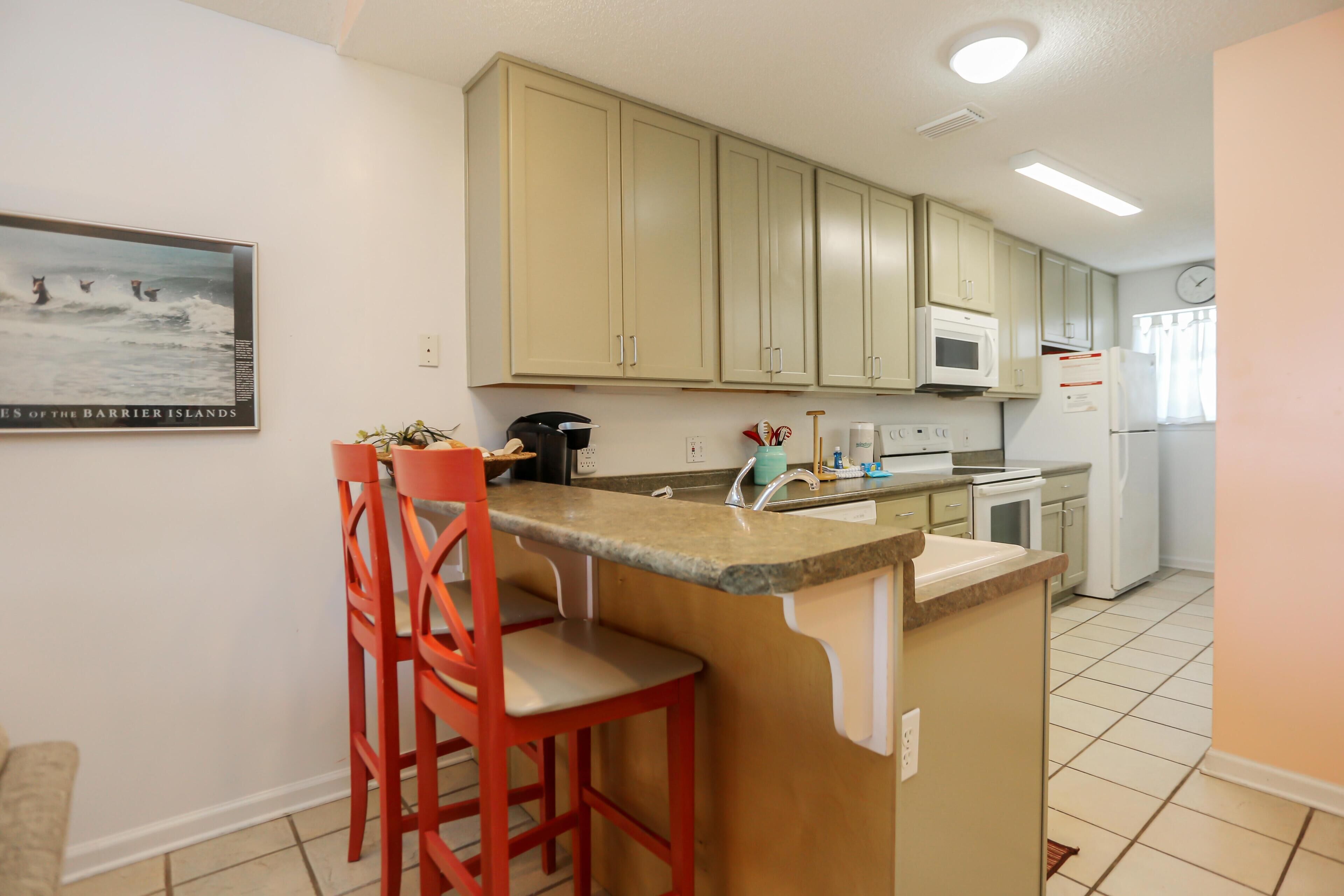 A kitchen with beige cabinets, a granite countertop, a sink, a microwave, a refrigerator, and a clock on the wall.