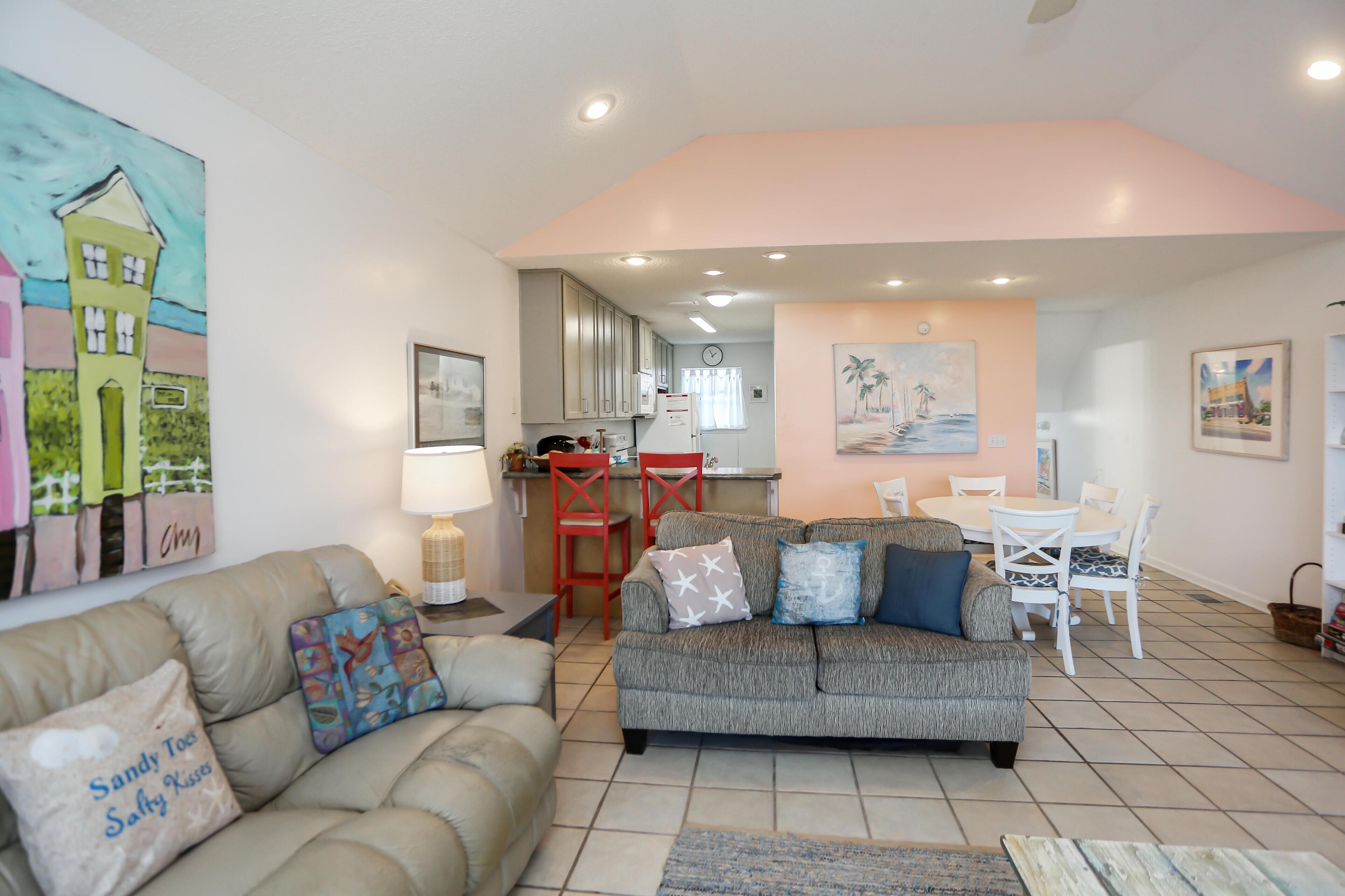 A living room with a sofa, a dining table with chairs, and a kitchen area in the background.