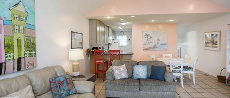 A living room with a sofa, a dining table with chairs, and a kitchen area in the background.
