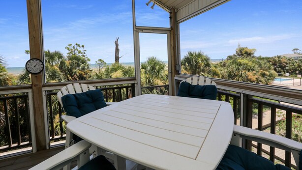 A covered outdoor deck with a table and chairs, overlooking a beach and pool area. - 2-The-Beach (Port St. Joe)