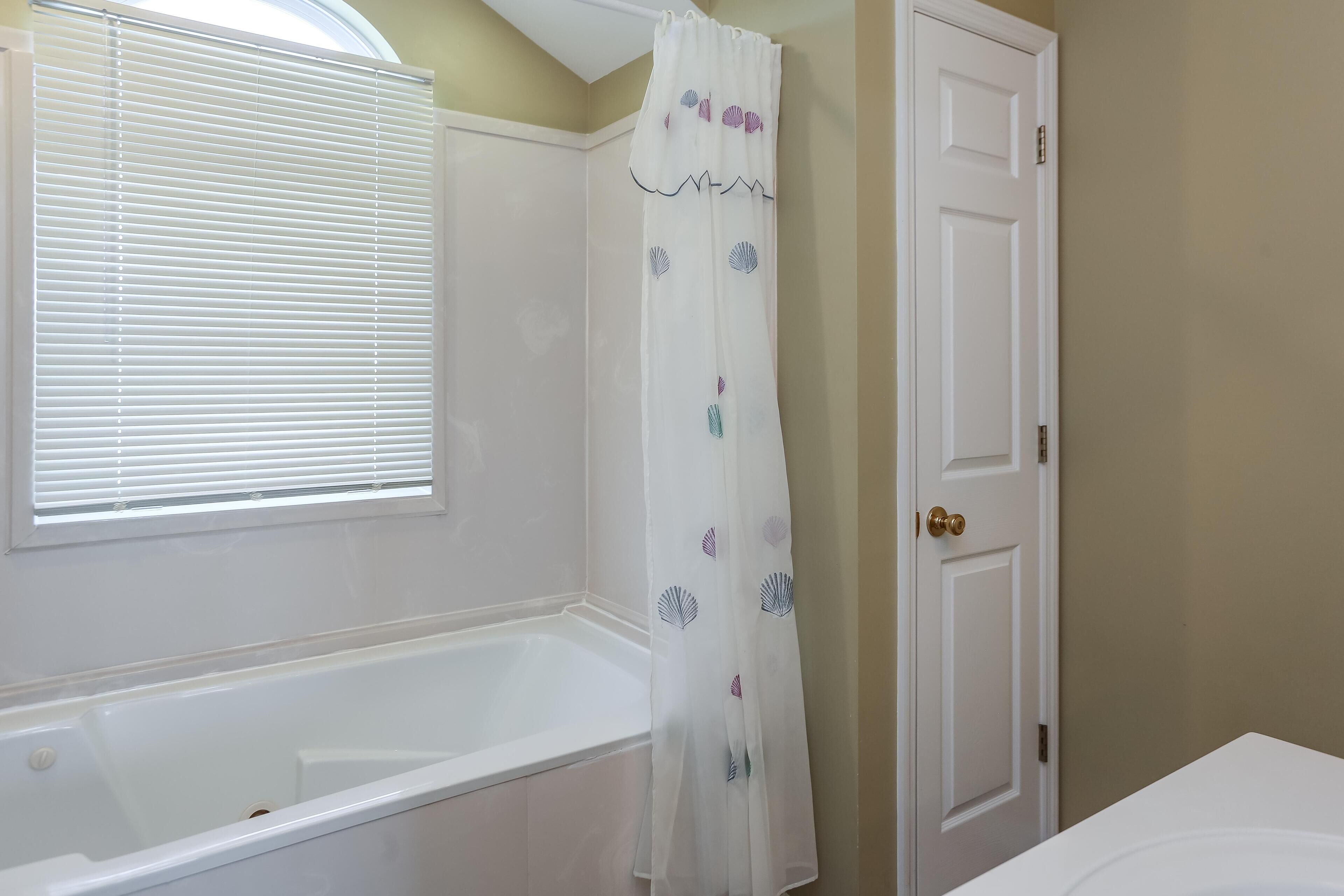 A bathroom with a bathtub, a shower curtain with a scalloped edge, and a door with a brass doorknob.