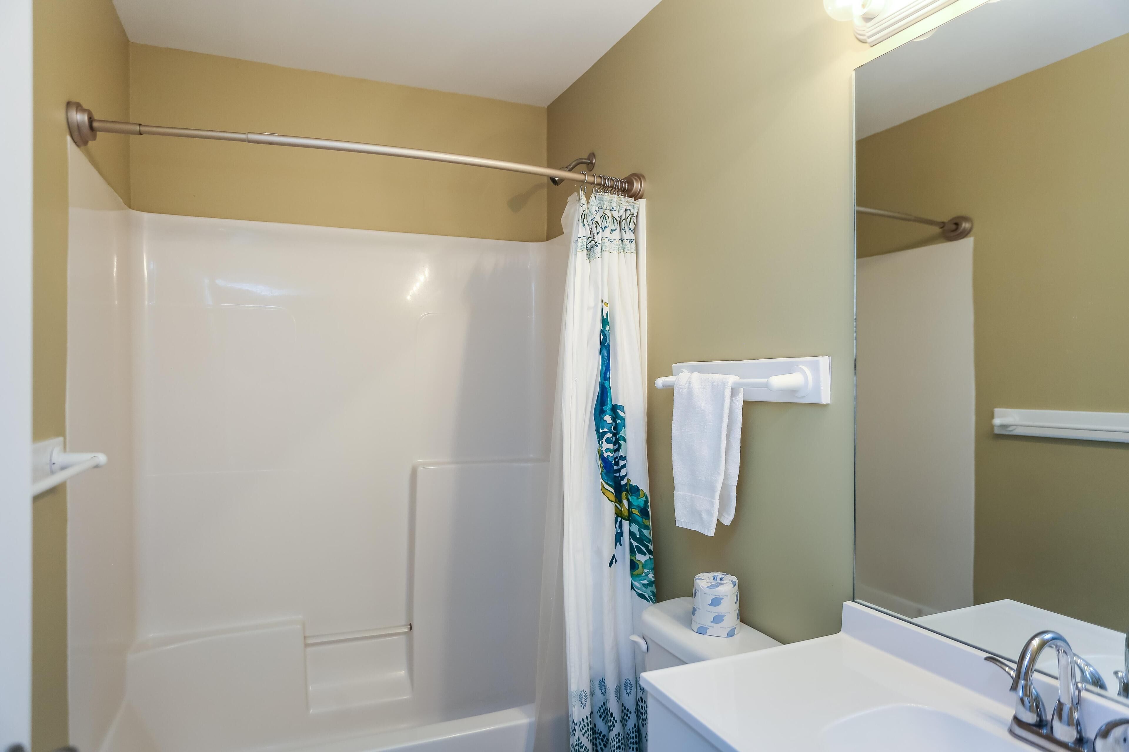 A bathroom with a shower, toilet, sink, and mirror.