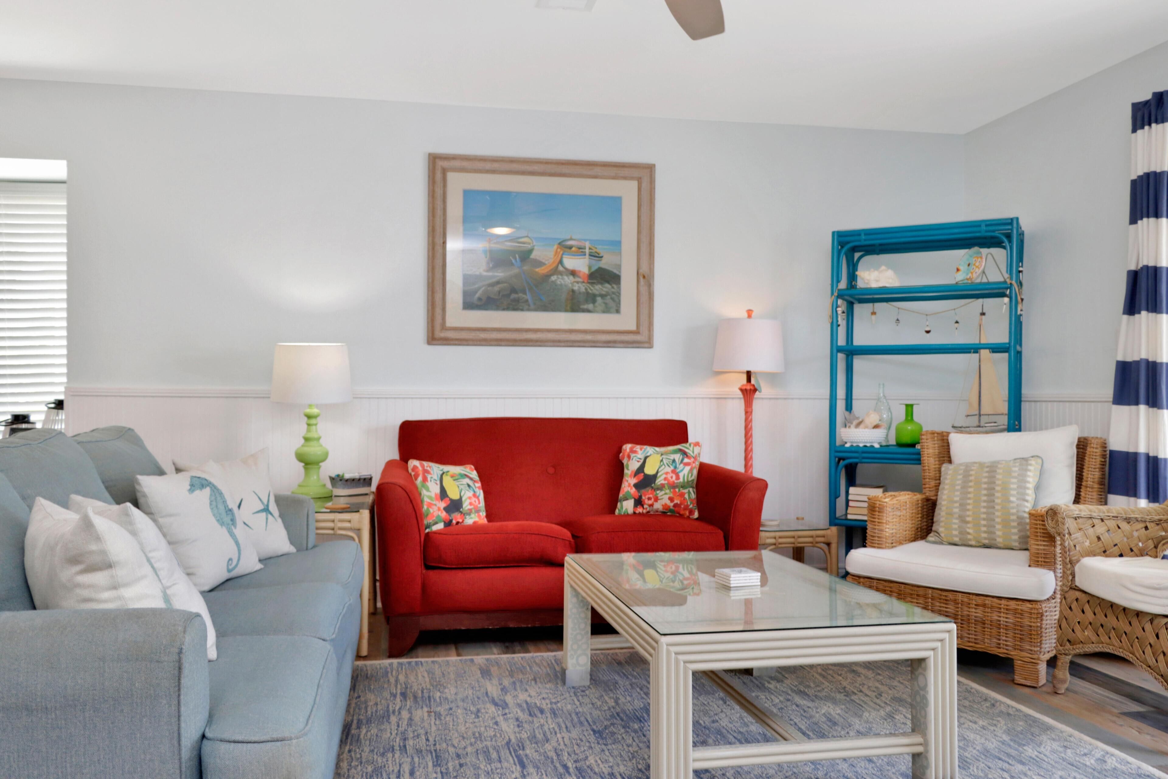 Una sala de estar con un sofá rojo, un sillón azul y una mesa de centro de vidrio.