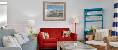 Una sala de estar con un sofá rojo, un sillón azul y una mesa de centro de vidrio.
