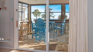 A room with a sliding glass door leading to an outdoor deck with blue chairs and a table. - Gulfside GEM (Port St. Joe)