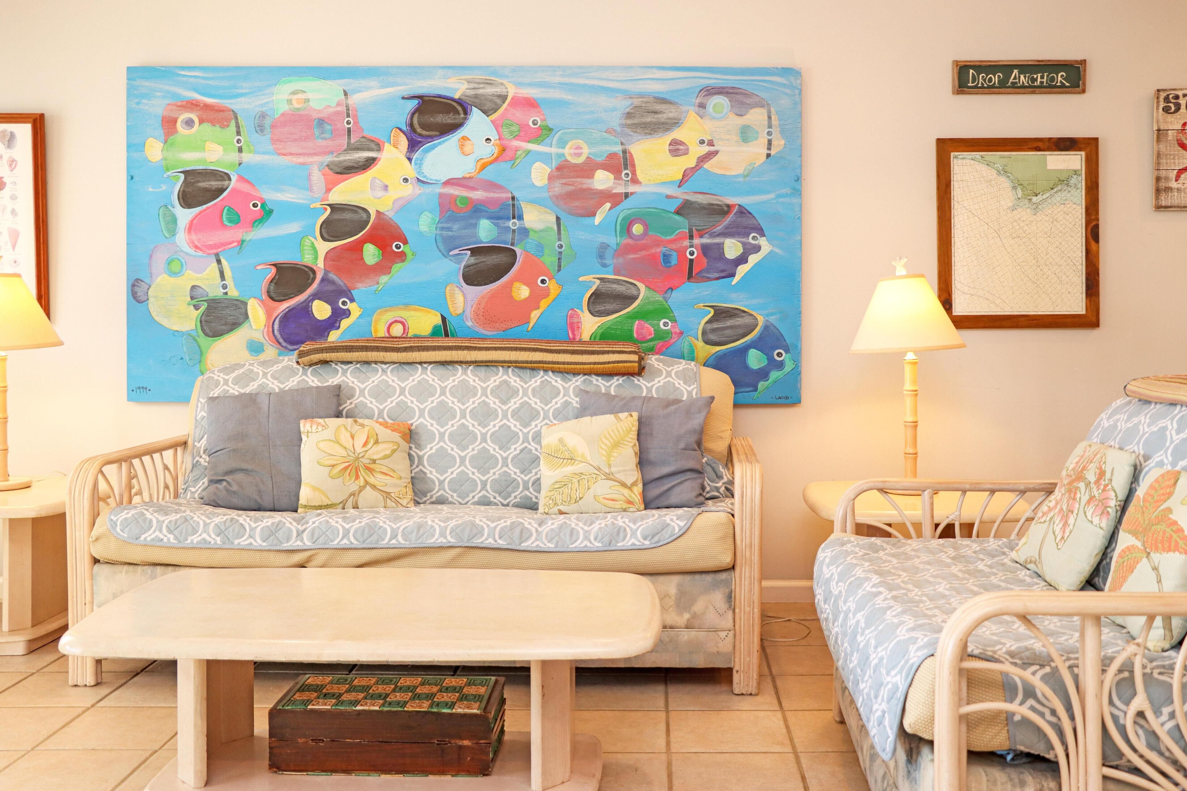 A room with a sofa, a small table, a map on the wall, and a painting of fish.