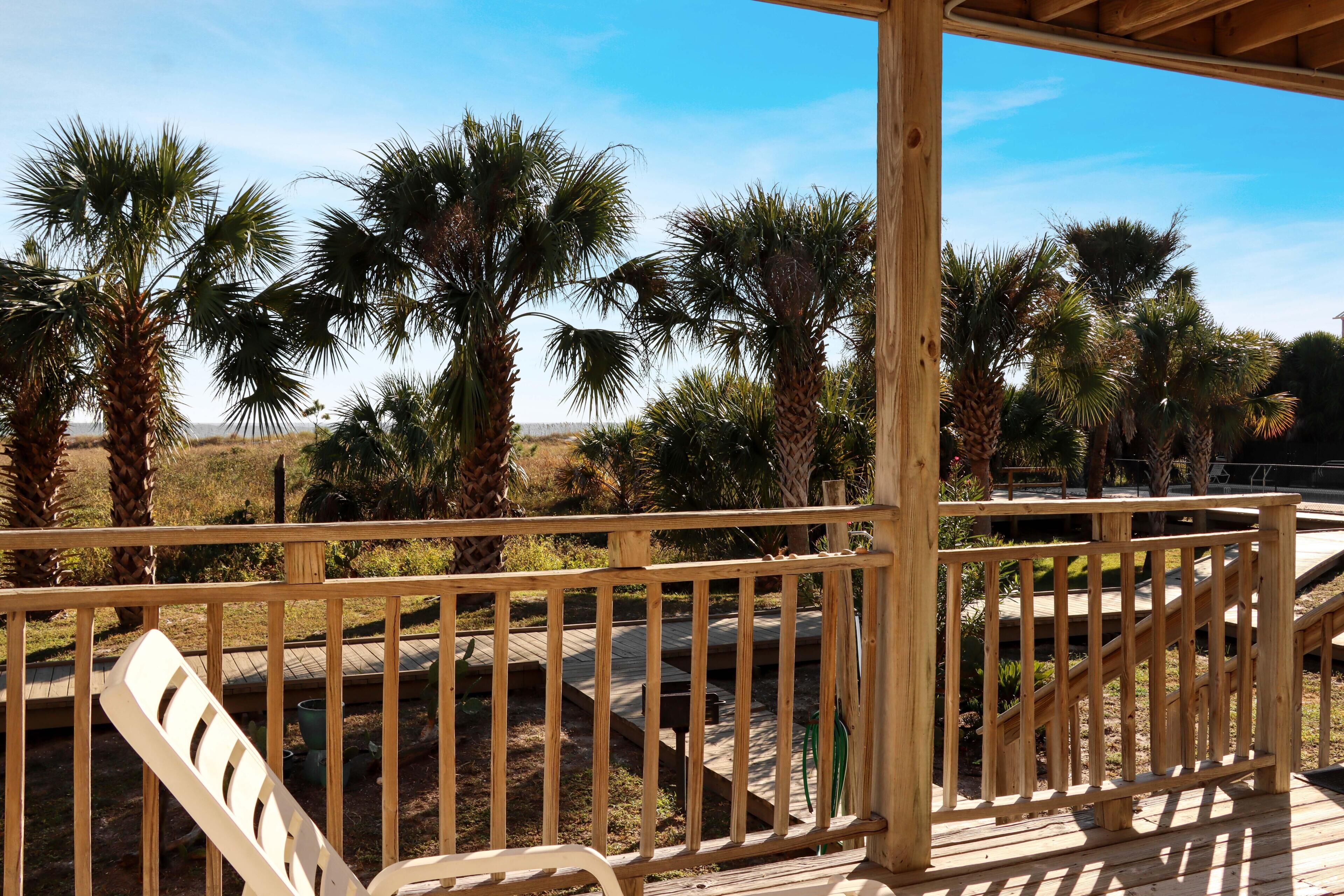 A wooden deck with a railing, palm trees, and a clear sky.