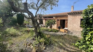 Una casa rustica con tetto in tegole, un'amaca e un barbecue in giardino.