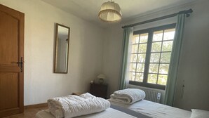 Una camera da letto con due letti, una porta in legno, uno specchio, una finestra con tende e un lampadario.