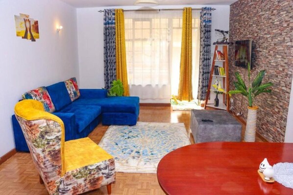 A living room with a blue sofa, a patterned armchair, a round wooden table, and a bookshelf.