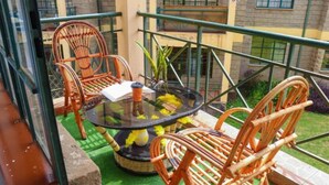 Een balkon met rieten stoelen, een glazen tafel en een plant in pot.