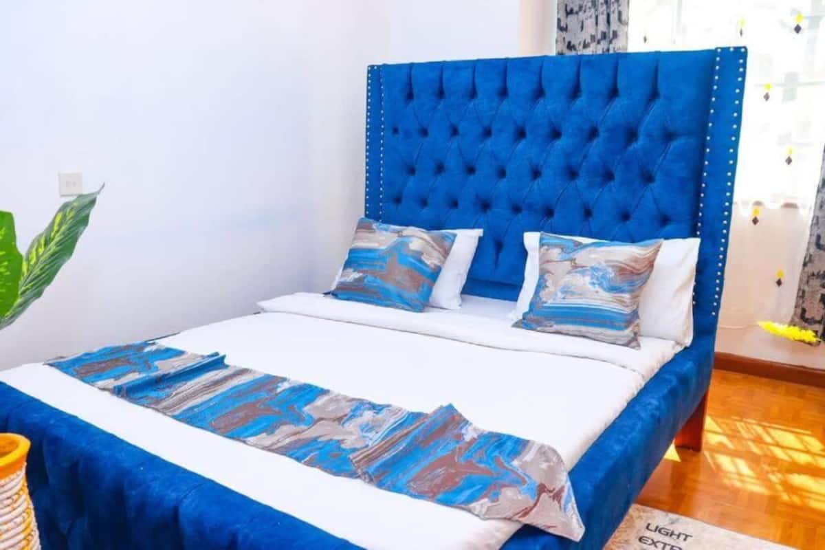 Un lit avec une tête de lit bleue, une literie blanche et des coussins à motifs.