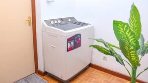 Een compacte, witte wasmachine in een hoek van een kamer met houten vloeren en een plant in pot.