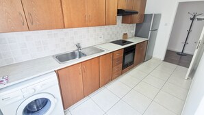 A modern kitchen with wooden cabinets, a built-in oven, and a washing machine. - Island Time Holiday Apartment (Larnaca)