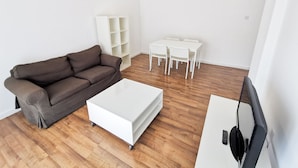A modern living room with a brown sofa, a white coffee table, and a TV stand. - Island Time Holiday Apartment (Larnaca)