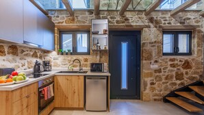 Eine moderne Küche mit Steinwänden, Holzbalken, einem Backofen, einem Geschirrspüler und einem kleinen Fenster.