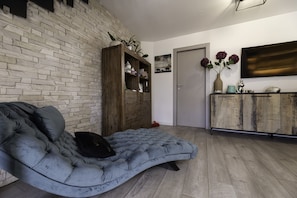 Una sala de estar con un sofá capitonado gris, un mueble de madera y una pared de ladrillo.