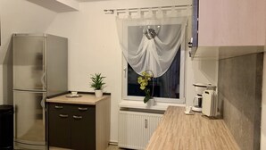 A compact kitchen with a built-in refrigerator, a small countertop, and a window with sheer curtains. - Beautiful vacation apartment "Bella" in the forester's lodge (Kröslin)