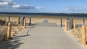 A paved walkway leading to a beach with a clear sky and distant shoreline. - Beautiful vacation apartment "Bella" in the forester's lodge (Kröslin)