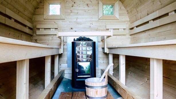 A sauna room with wooden walls, a black sauna door, and a wooden bucket with a ladle. - Beautiful vacation apartment "Bella" in the forester's lodge (Kröslin)