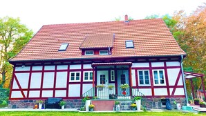 A traditional half-timbered house with a red-tiled roof, a front porch with potted plants, and a small garden area. - Beautiful vacation apartment "Bella" in the forester's lodge (Kröslin)
