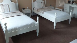 Une chambre d’hôtel avec deux lits blancs, un bureau, une chaise, un tableau au mur et un miroir.