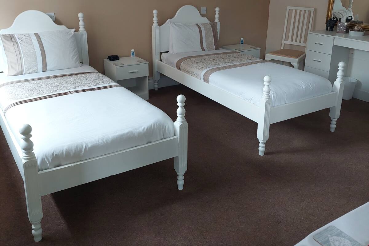 A hotel room with two white beds, a desk, a chair, a painting on the wall, and a mirror.