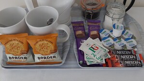 Un coin café équipé d’une machine à café, de tasses, d’un pot à lait et de différents types de dosettes de café.