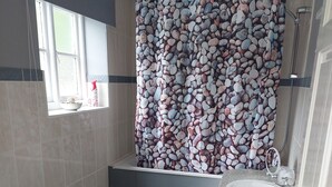 Une salle de bain avec un rideau de douche orné d’un motif de petits galets, un lavabo et des toilettes.
