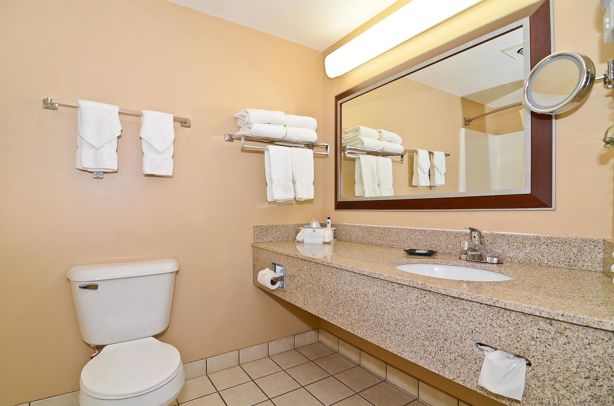 A hotel bathroom with a toilet, sink, and multiple towel racks.