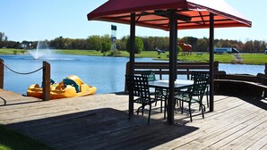 A wooden deck with a gazebo, yellow paddle boats, and a view of a lake with a fountain and a horse statue. - Quality Inn & Suites Black River Falls I-94 (Black River Falls)