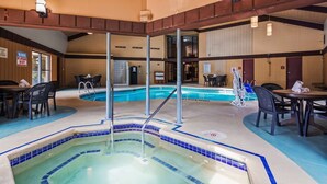 An indoor swimming pool with a hot tub, surrounded by tables and chairs, and a lifeguard on duty sign. - Quality Inn & Suites Black River Falls I-94 (Black River Falls)