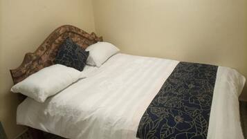 Un letto con una testiera in legno, biancheria da letto bianca e una coperta con motivi floreali blu.