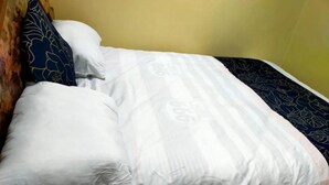 A neatly made bed with white bedding and a dark blue floral-patterned pillow.